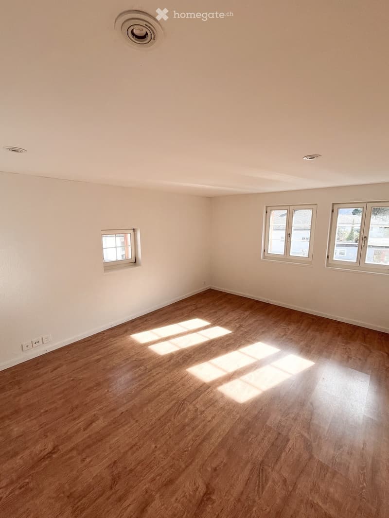 Empty room with wooden flooring and white walls, featuring multiple windows allowing natural light to enter.
