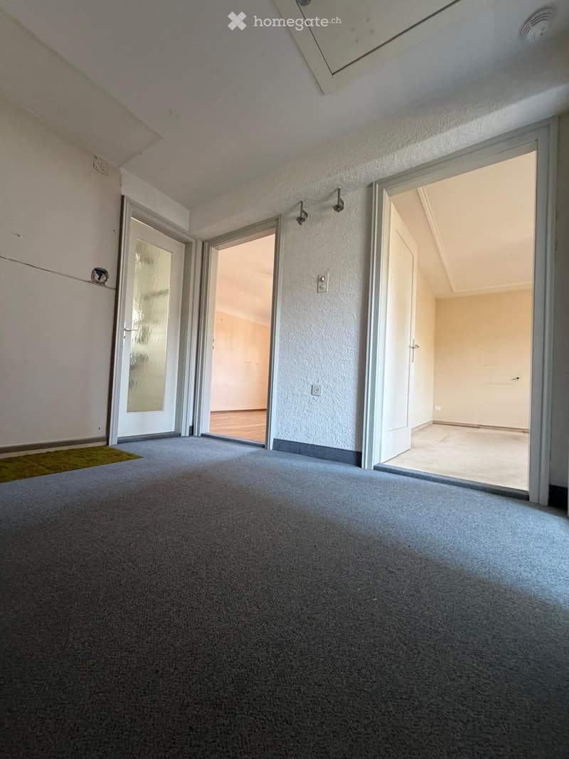 Empty room with grey carpet, white walls, and multiple open doors leading to other spaces.
