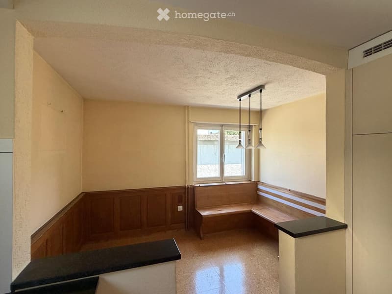 Empty room with beige walls, wooden paneling, built-in benches, and a window with a view of the outside.