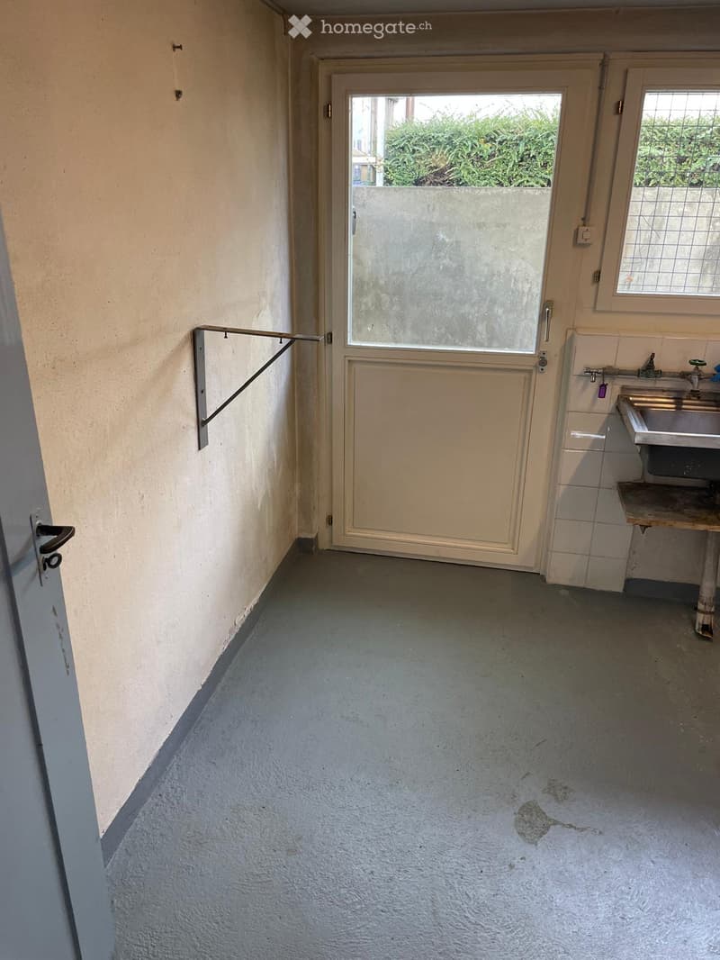 Empty hallway with a door leading to an outdoor area, a sink, and a window with bars.