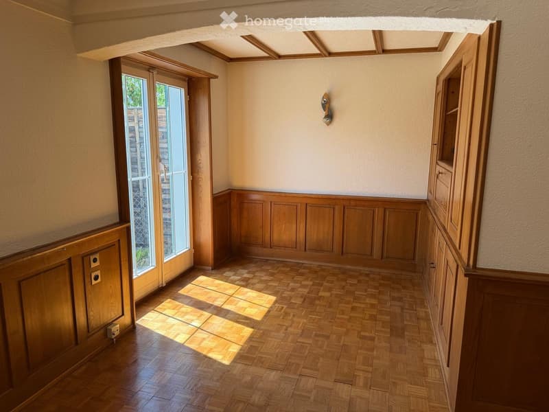 Empty hallway with wooden paneling, wooden floor, and large window letting in natural light.