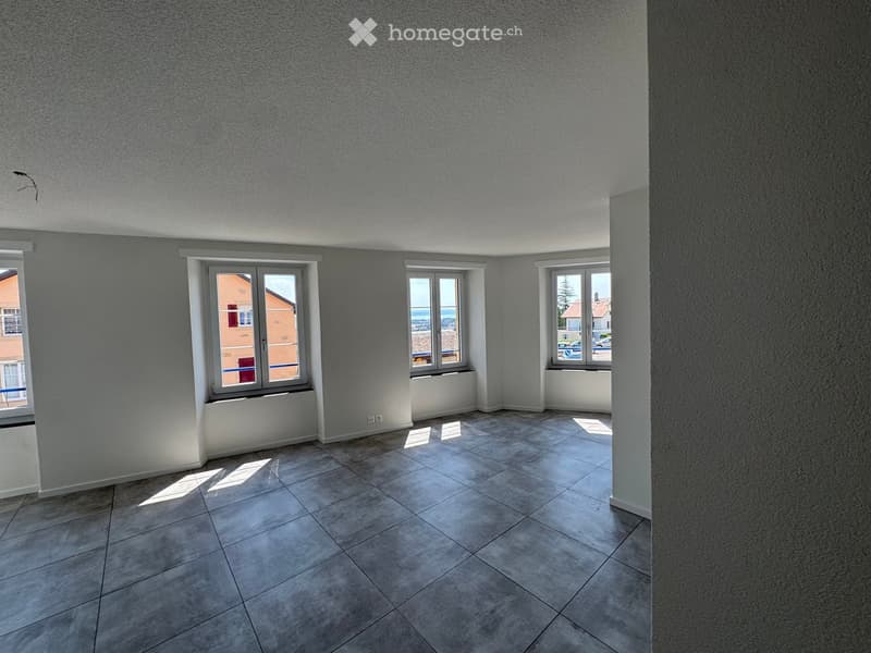 Empty room with tiled floor, grey walls, and three windows offering views of the outside.