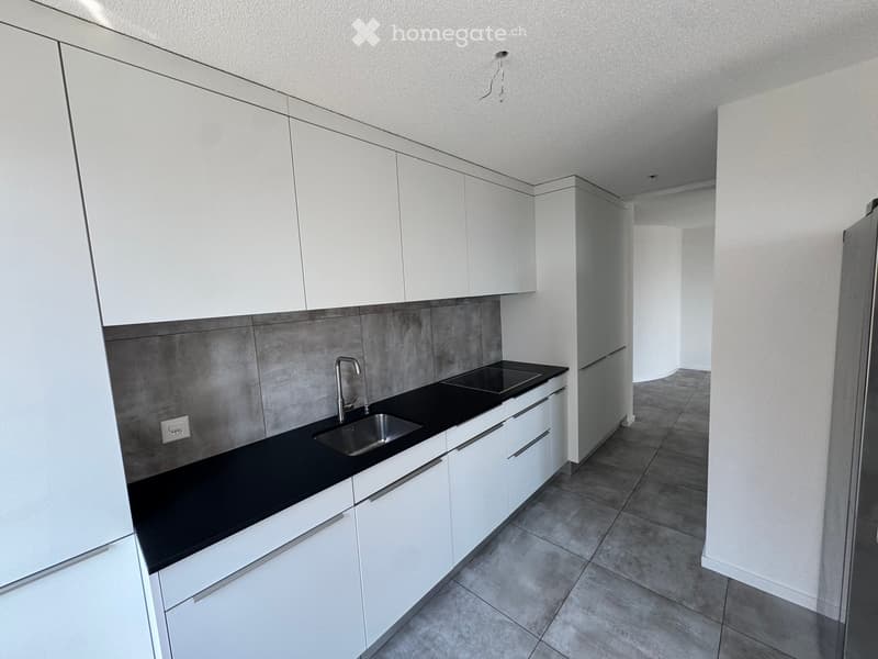 Modern kitchen with white cabinets, black countertops, and a stainless steel sink.