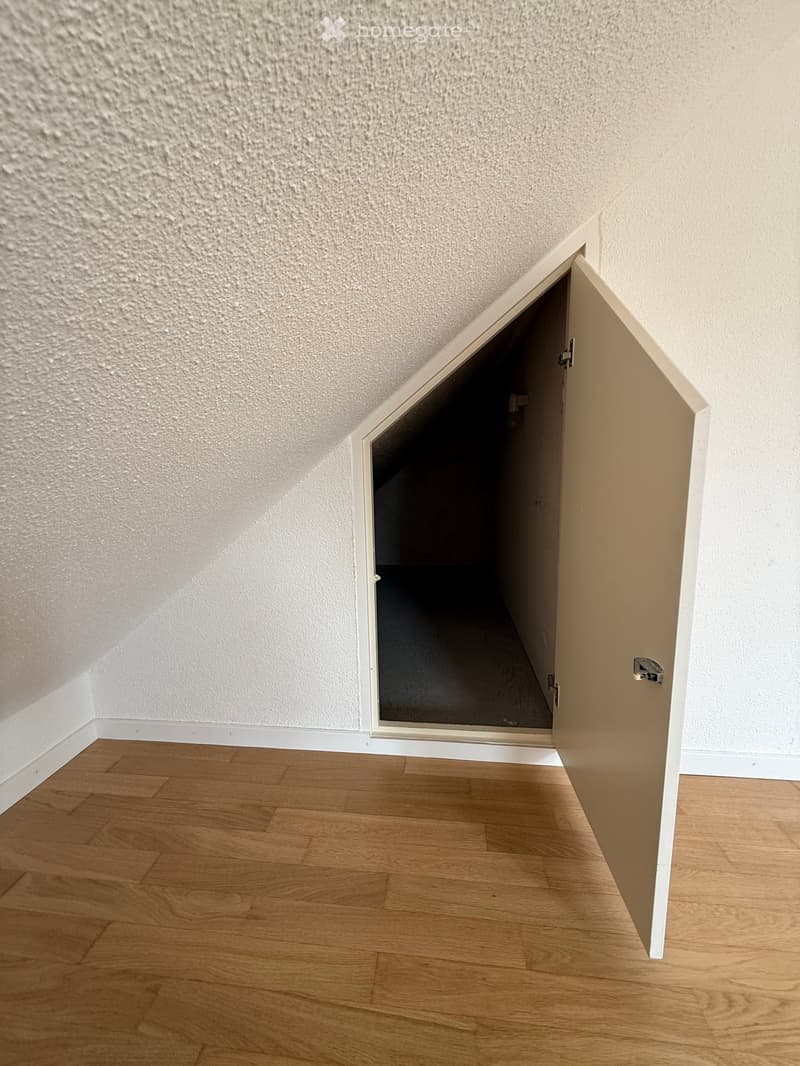 Empty room with wooden flooring and white walls, featuring an open door leading to another space.