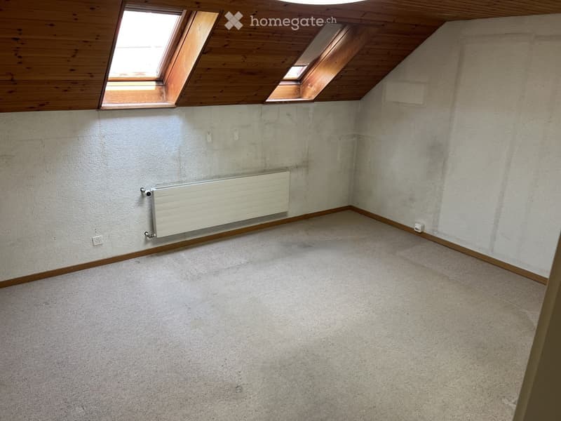 Empty room with concrete walls, carpeted floor, wooden ceiling, and skylight windows. Features a radiator on one wall and electrical outlets.
