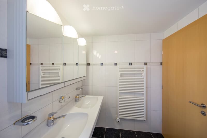 Modern bathroom with white tiles, a double sink, a large mirror, a white radiator, and a wooden door.
