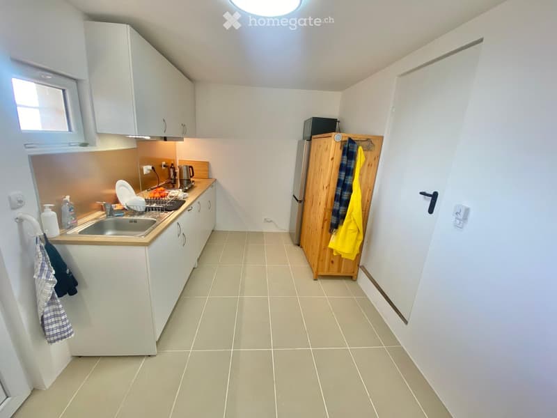 Modern kitchen with white cabinets, a stainless steel sink, a wooden cabinet, and a refrigerator. The countertop has a dish rack, a kettle, and various kitchen items.
