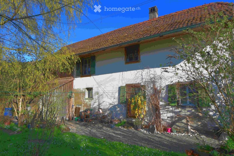 Traditional house with red roof, white walls, green shutters, garden with plants and trees, outdoor seating area with table and chairs