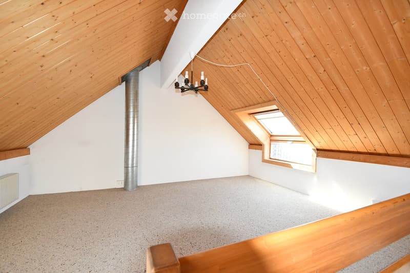 Empty attic space with wooden slanted ceilings, white walls, carpeted floor, skylight window, and exposed metal pipe.