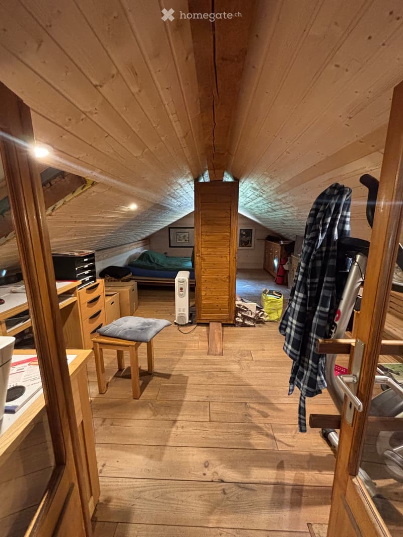 Cozy attic room with wooden walls and slanted ceilings, featuring a bed, wardrobe, small table, and a heater.