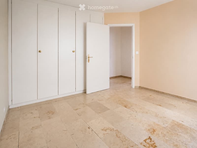Empty room with beige tiled flooring, white walls, and built-in white closet units. A doorway leads to another room.