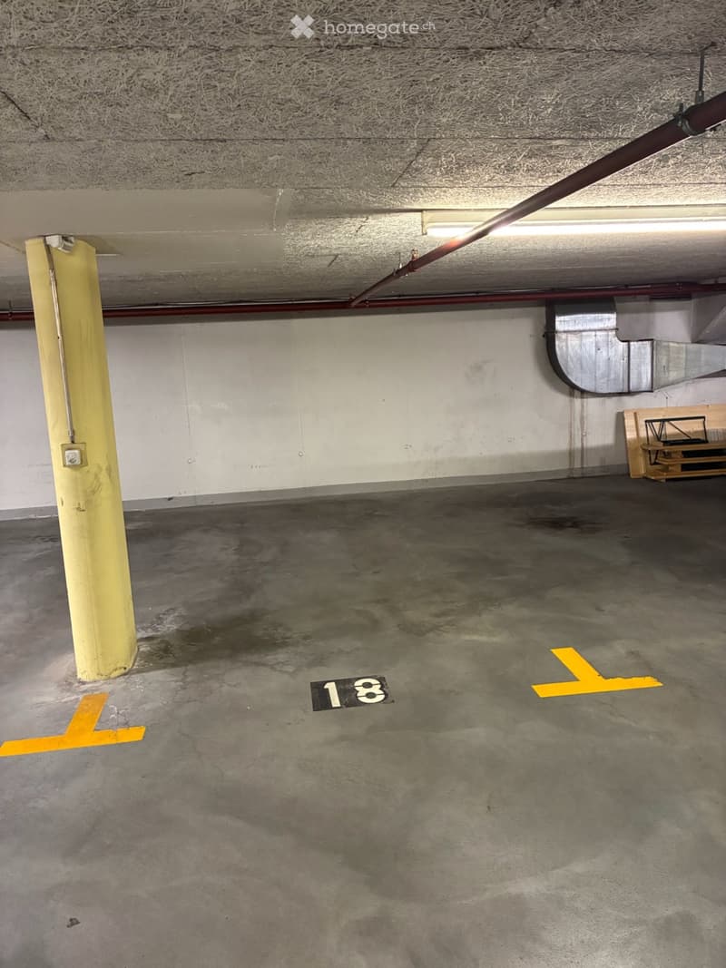 Underground parking space with concrete floor, yellow painted lines, and a numbered parking spot (18).