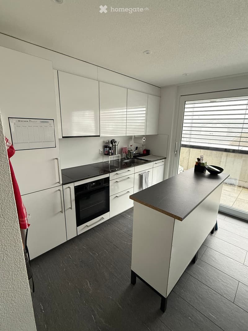 Modern kitchen with white cabinets, black countertop, stainless steel appliances, and a large window with blinds.