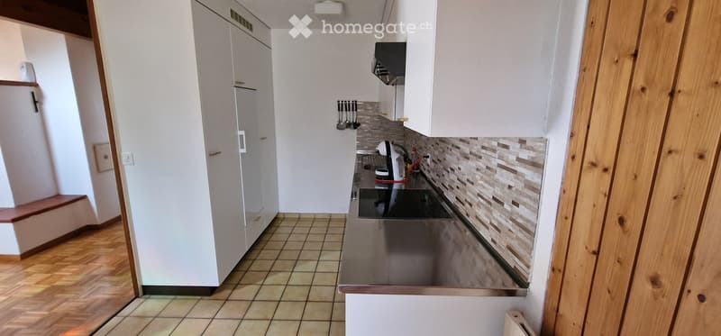 Modern kitchen with white cabinets, stainless steel appliances, and a tiled backsplash. The space features a wooden floor and a built-in stove with a sink nearby.