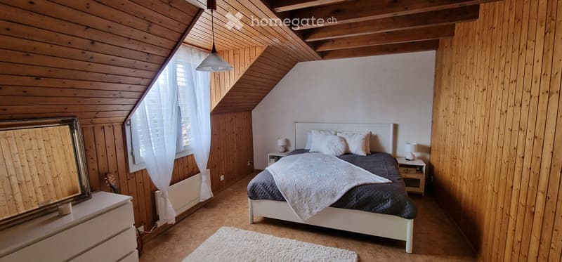 Cozy attic bedroom with wooden walls and ceiling, featuring a bed with white pillows and a dark blue duvet, nightstands with lamps, a mirror, and a guitar leaning against the wall.