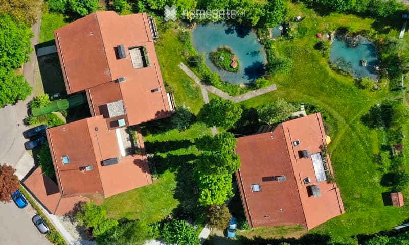 Aerial view of a residential complex with three buildings, surrounded by green lawns, trees, and a small swimming pool.