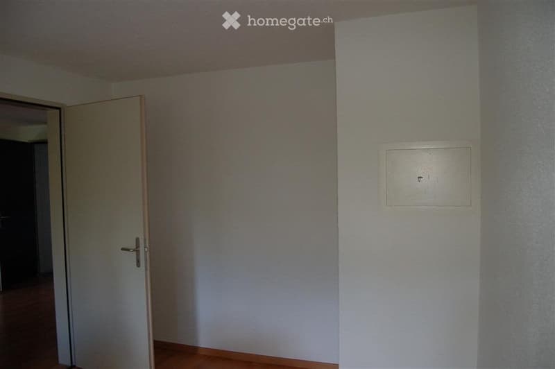 Empty room with wooden flooring, white walls, and a closed door leading to another space.