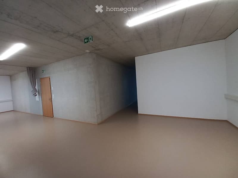 Empty room with concrete walls, wooden door, and fluorescent lighting. No furniture or equipment present.