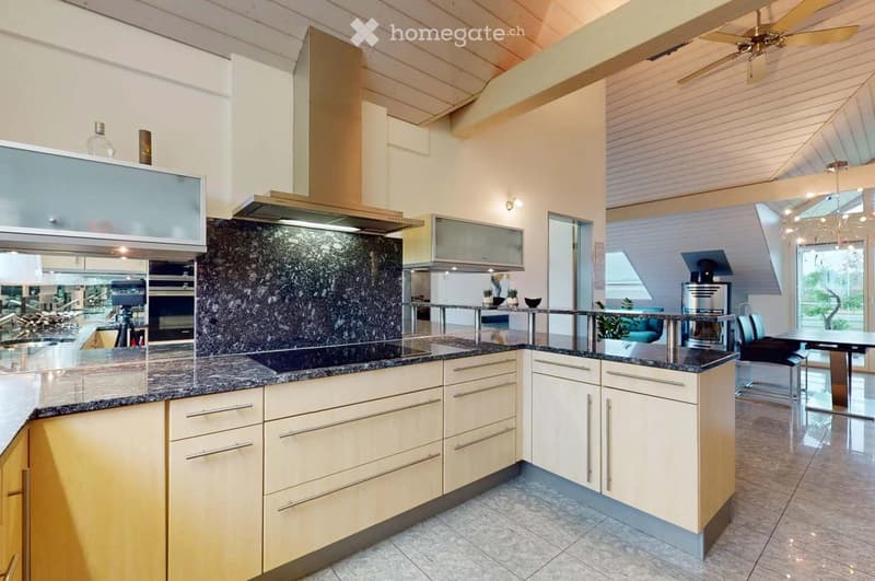 Modern kitchen with granite countertops, light wood cabinets, stainless steel range hood, and a dining area with a table and chairs.
