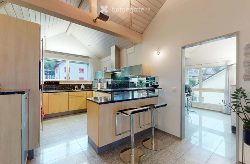 Modern kitchen with a central island, light-colored cabinets, and a black countertop. Two high stools are placed at the island, and the space features large windows and a sleek design.