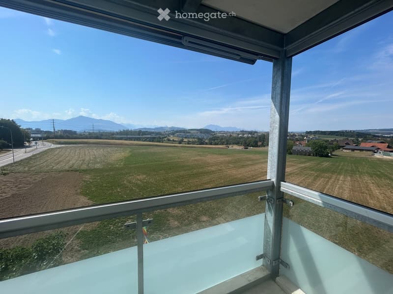 Balcony with metal railing, offering a panoramic view of a rural landscape, fields, and distant mountains.