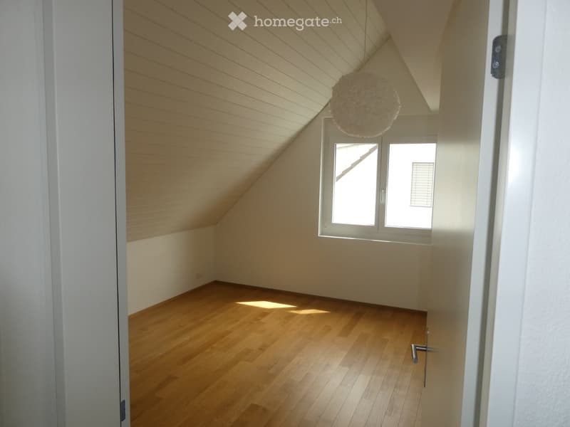Empty attic room with wooden floors, white walls, and a skylight window. The room features exposed wooden beams on the ceiling and a hanging decorative ball light fixture.