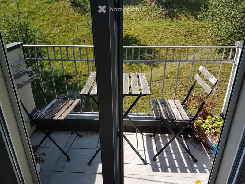 Balcony with tiled floor, metal railing, and several wooden folding chairs, overlooking a grassy hillside.