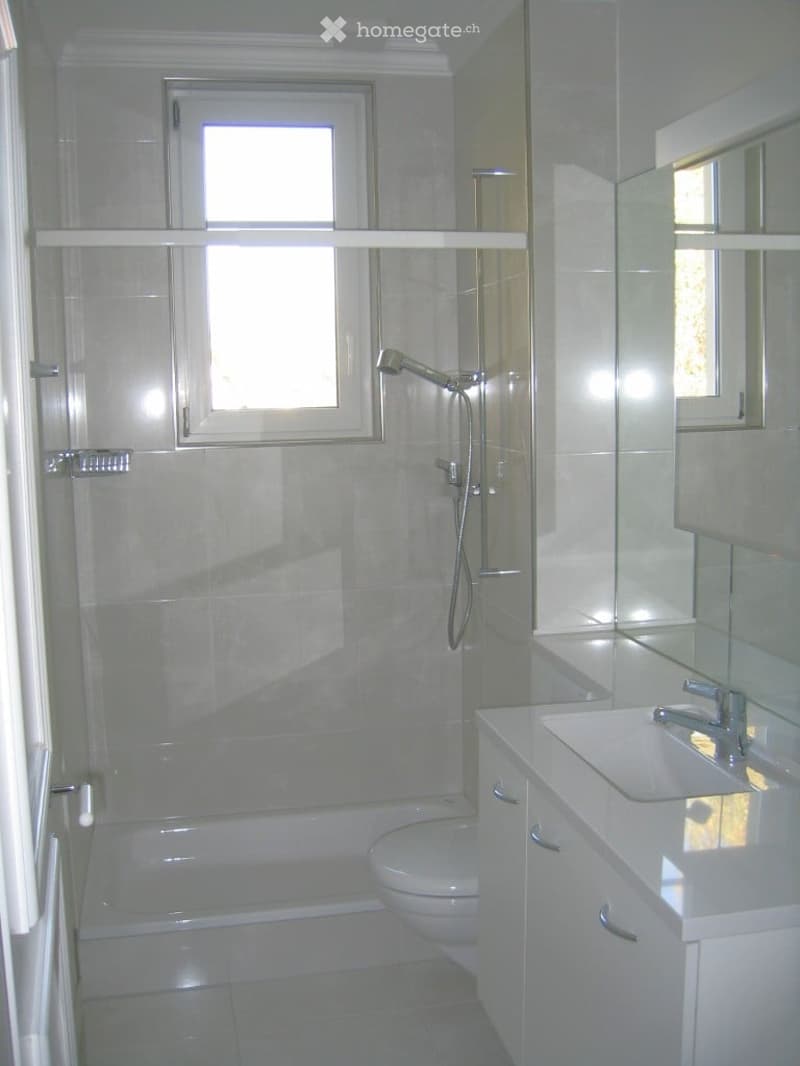 Modern bathroom with white tiles, a bathtub, toilet, sink, and a glass-enclosed shower area with a showerhead.