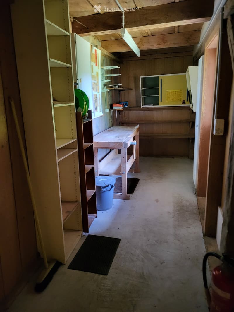 Empty hallway with wooden walls, exposed beams, shelves, and a workbench. No furniture or equipment.