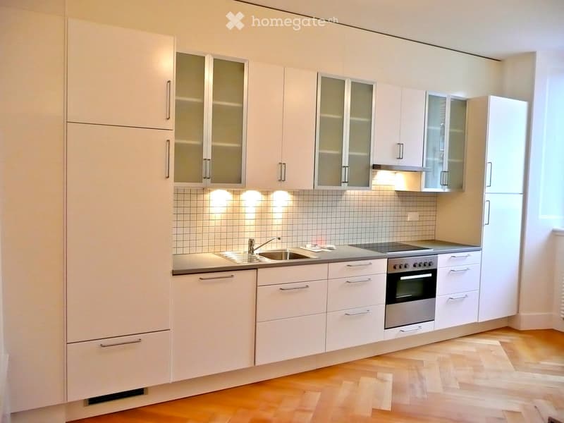 Modern kitchen with white cabinets, stainless steel sink, oven, and tiled backsplash.