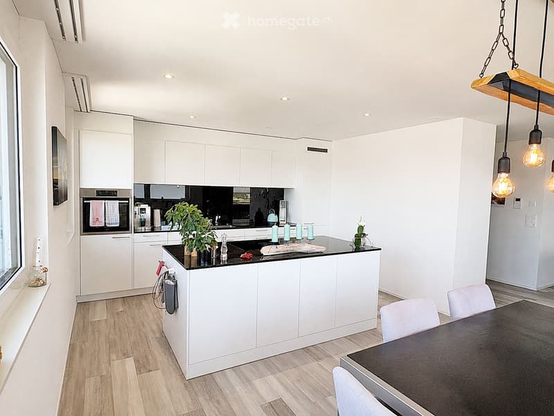 Modern kitchen with white cabinets, black countertop, island, dining table, and pendant lights.
