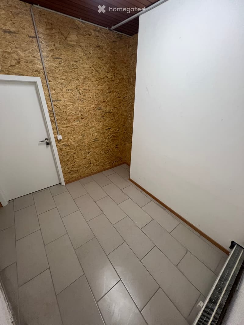 Empty room with tiled floor, white walls, and a wooden panel wall section. No furniture or equipment present.