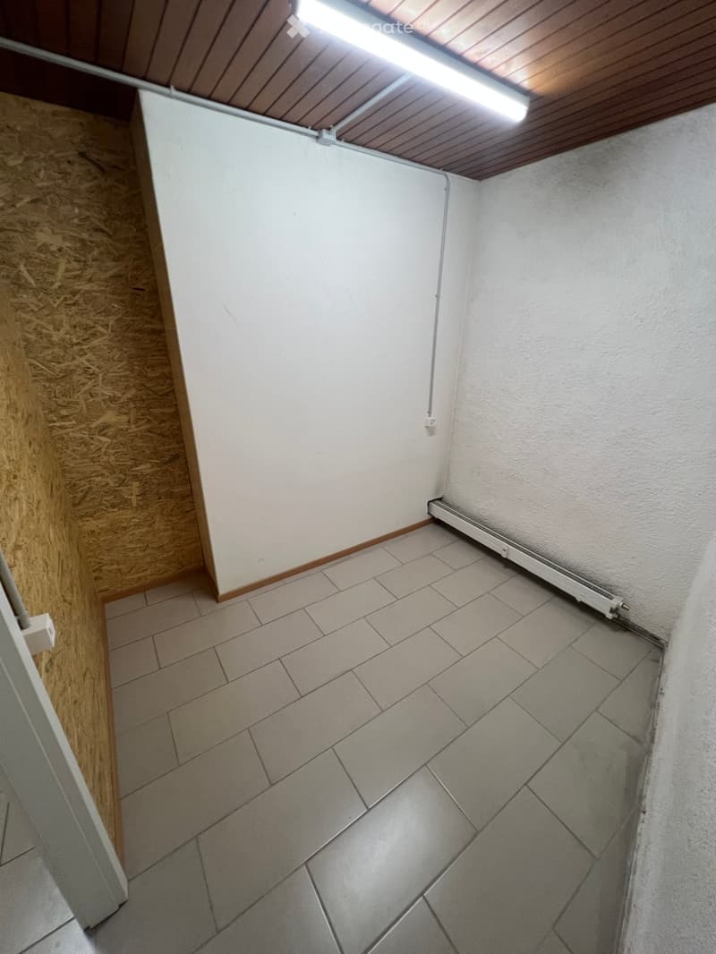 Empty room with tiled floor, white walls, and a wooden ceiling with a fluorescent light fixture. No furniture or equipment is present.