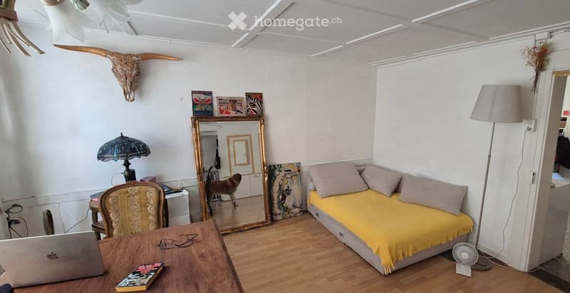 Cozy living room with a yellow sofa, wooden table, laptop, decorative mirror, and a floor lamp.