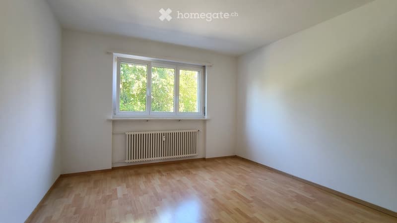 Empty room with wooden flooring, white walls, and a window with a radiator below it.