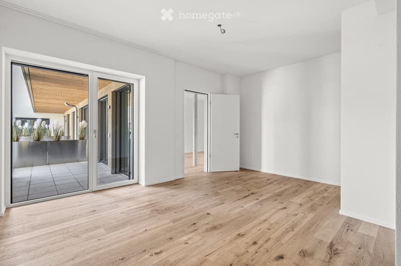 Bright, empty room with light wooden flooring, white walls, and large sliding glass doors leading to an outdoor area.