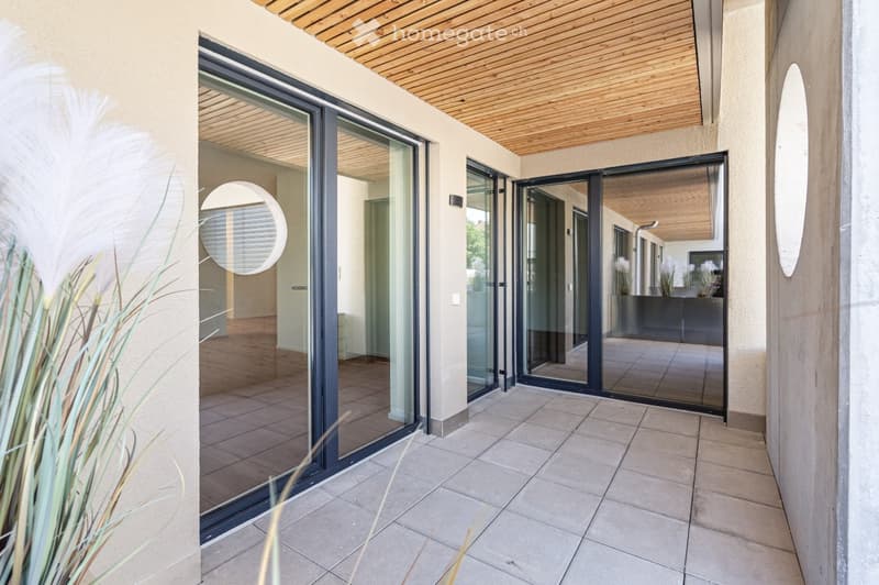 Modern balcony with large glass sliding doors, wooden ceiling, tiled floor, and circular mirrors on walls.