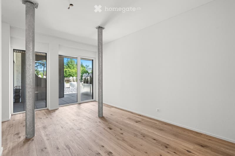 Empty room with light wooden flooring, white walls, and large glass doors leading to an outdoor area.