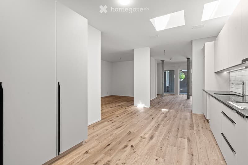 Bright, open corridor with light wooden flooring, white walls, and modern white cabinetry in the foreground. The space is empty, with no furniture or personal items visible.