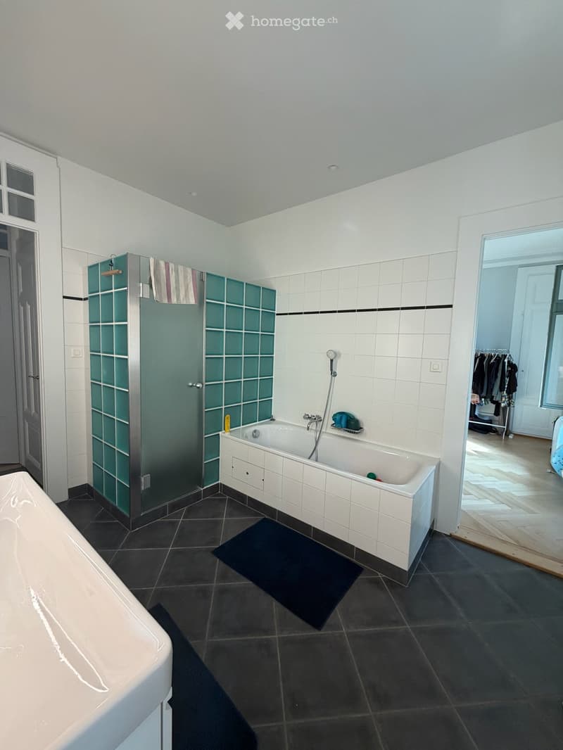 Modern bathroom with white tiled walls, dark tiled floor, bathtub, shower stall with glass doors, and a bathmat on the floor.