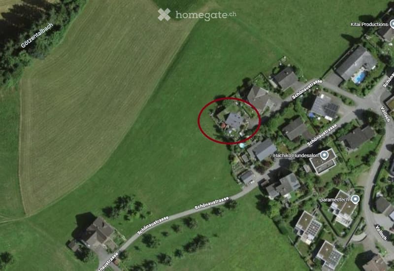 Aerial view of a residential area with multiple houses, surrounded by green fields and roads.