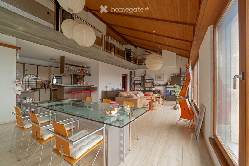 Open-plan living and dining area with a glass dining table, modern chairs, a sofa, kitchen area with counter and stools, and decorative items including a guitar and a flower vase.