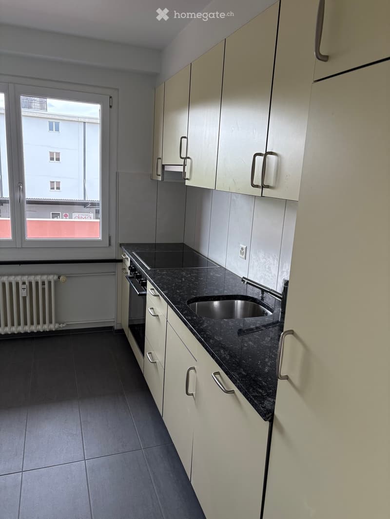 Modern kitchen with white cabinets, dark granite countertop, stainless steel sink, and built-in oven. Features a window with a view of a building.