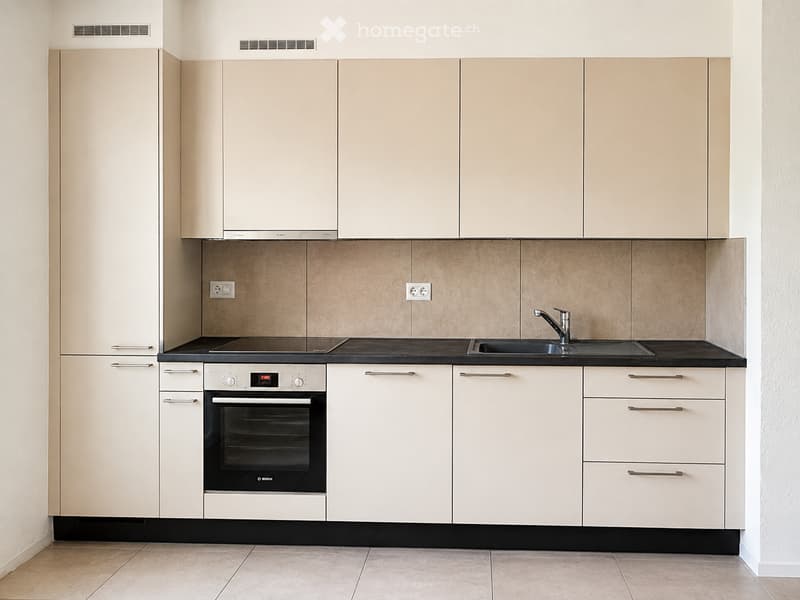 Modern kitchen with light-colored cabinets, black countertops, and stainless steel appliances including an oven and sink.