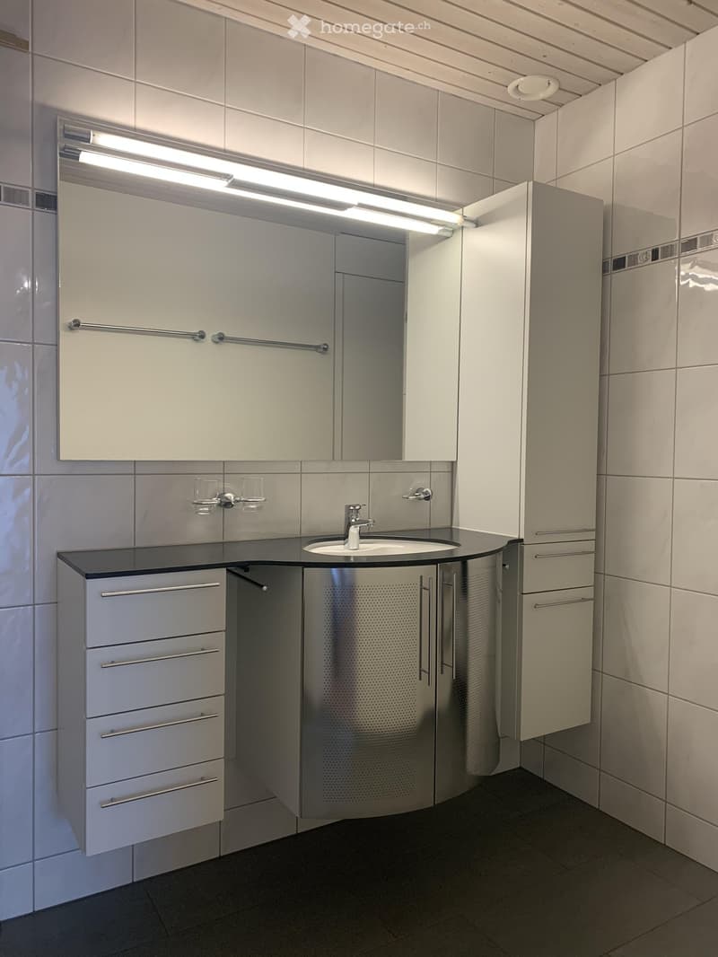 Modern bathroom with a white sink, mirror, and cabinets, featuring a sleek design and bright lighting.