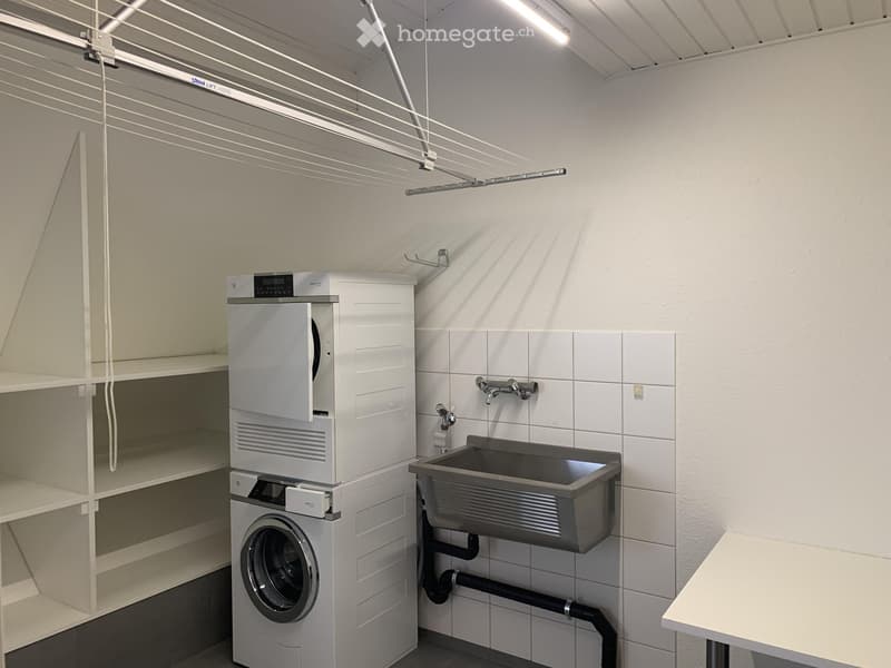 Modern bathroom with a washing machine, sink, and faucet, featuring white tiled walls and a drying rack.