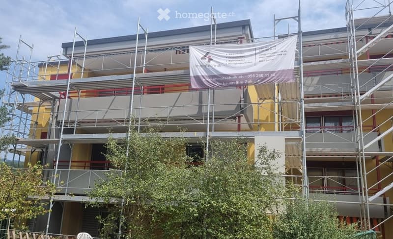 Multi-story building under construction with scaffolding, yellow facade, and a banner advertising renovation services.