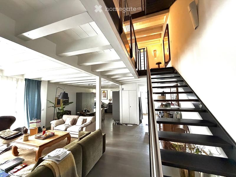 Open-plan living area with a staircase leading to an upper level, featuring a sofa, coffee table, chair, and decorative items.