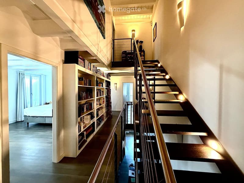 Spacious hallway with a wooden staircase leading to an upper level, featuring built-in bookshelves and modern lighting.