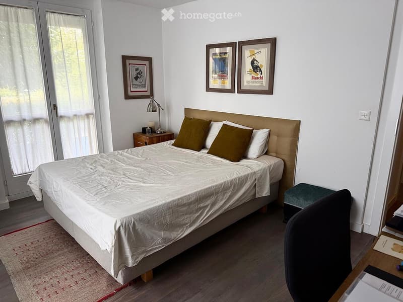 Cozy bedroom with a large bed, nightstand, lamp, framed pictures, and a small stool near the bed.